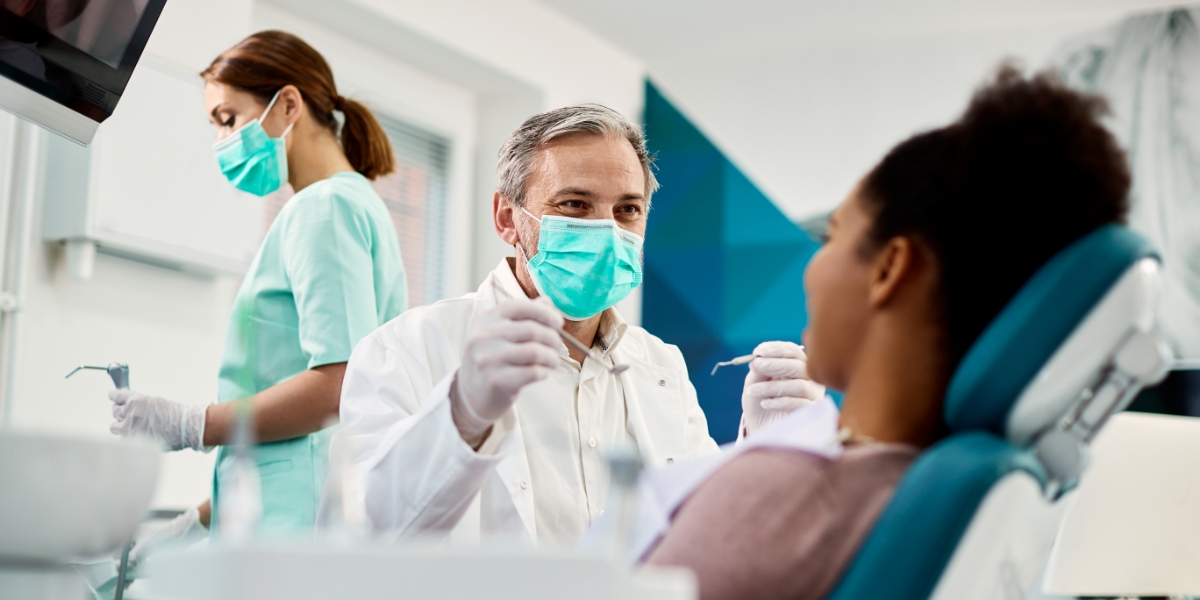 oral surgeon smiling with a mask on at patient looking up at him in a patient chair at saline oral facial and dental implants surgery