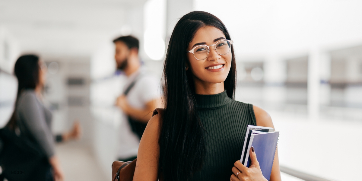 young woman smiling at the camera from a far holding a notebook at school after wisdom tooth removal at saline oral facial and dental implant surgery 1